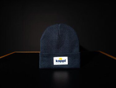 Eine blaue Mütze mit einem Etikett. Sie steht auf einem schlichten, dunklen Hintergrund.