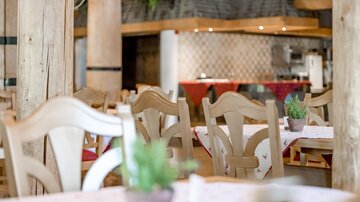 Ein einladendes Restaurant mit Holzstühlen und gedeckten Tischen. Im Hintergrund sieht man eine gemütliche Küchenzeile.