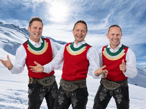 Ein Skifahrer fährt die Piste hinunter. Im Hintergrund sind schneebedeckte Berge und ein klarer Himmel zu sehen.