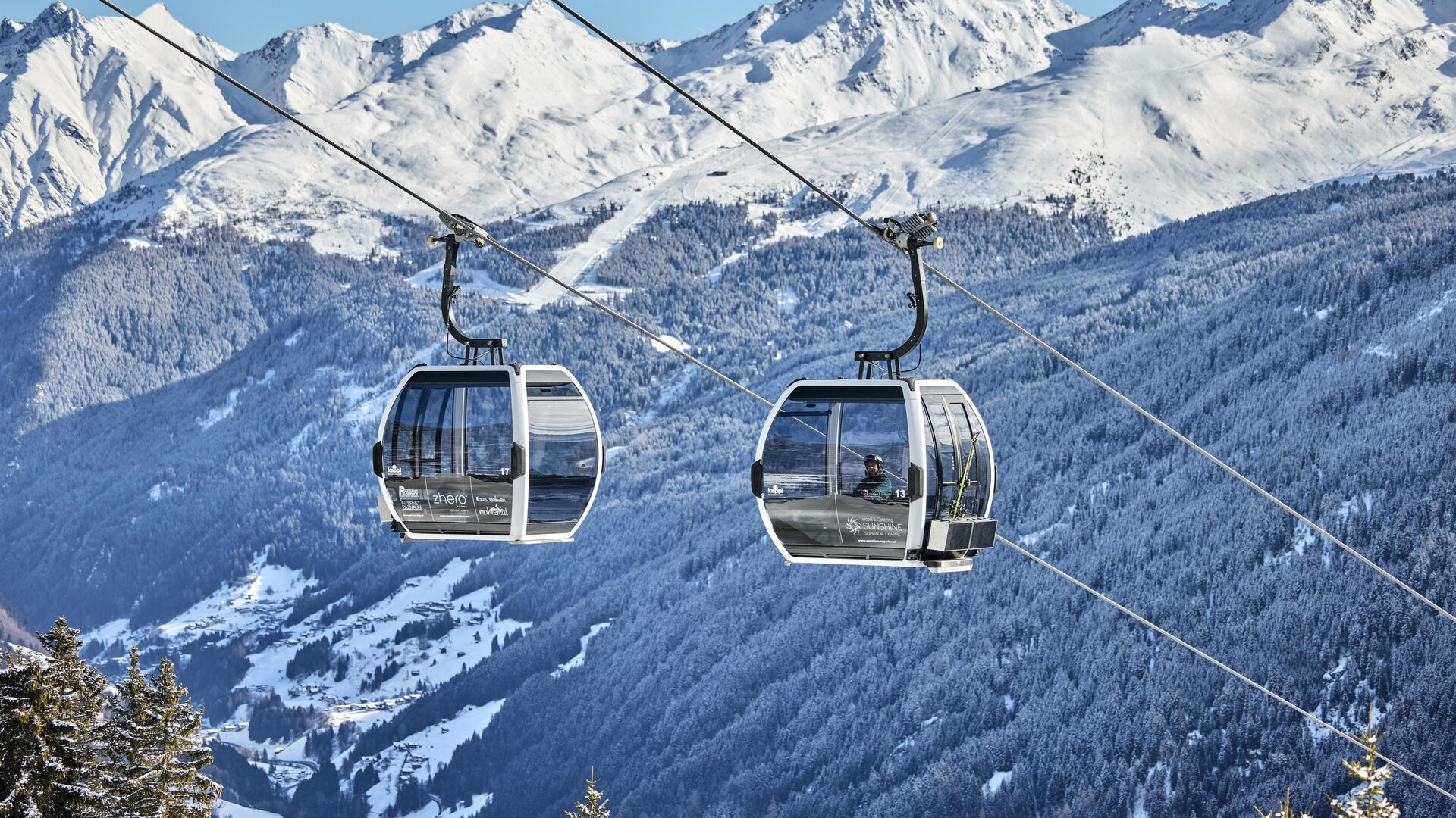 Ein Skifahrer fährt über eine schneebedeckte Piste in den Bergen. Im Hintergrund sind majestätische Berge und ein klarer Himmel zu sehen.