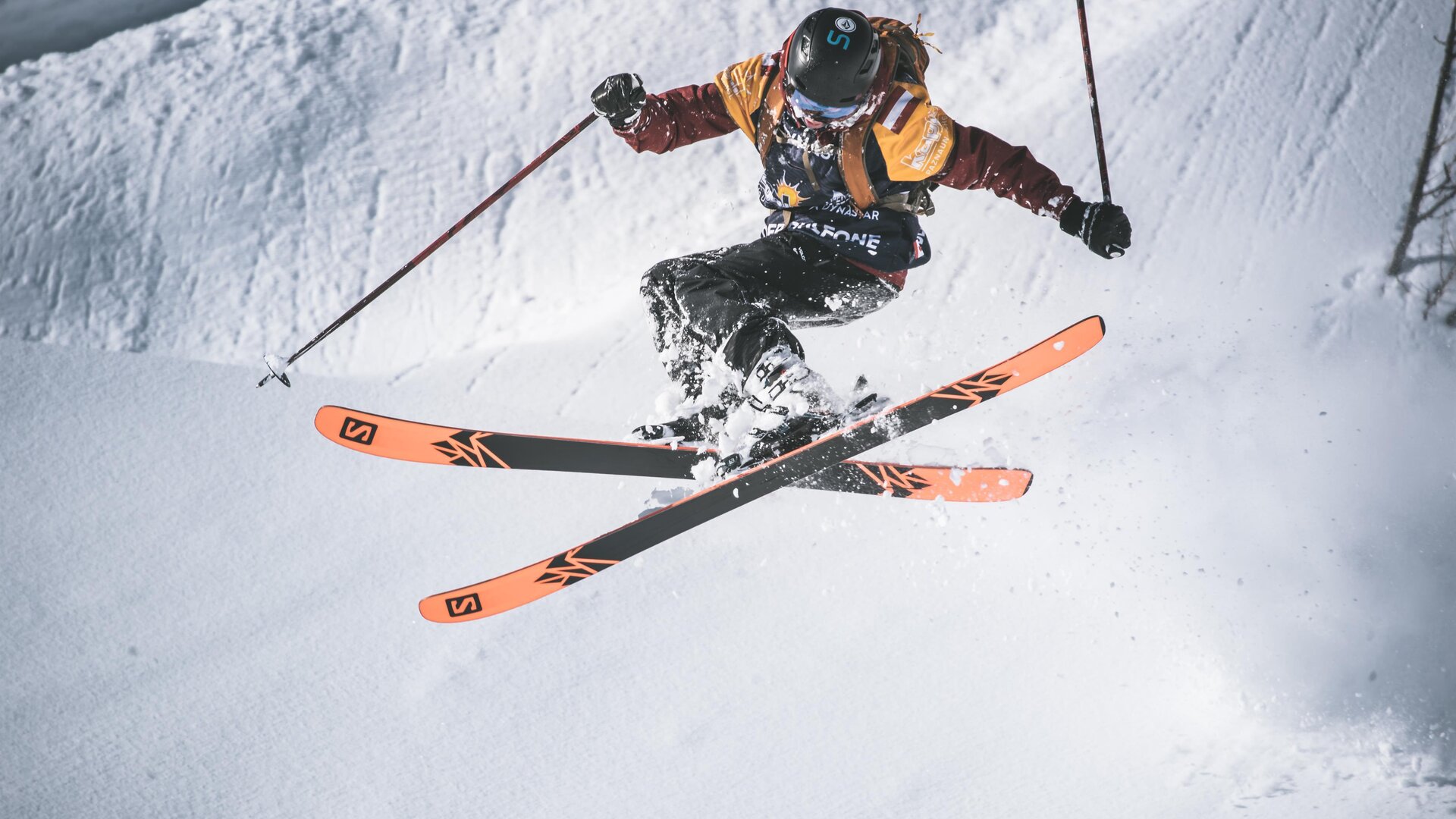 Ein Skifahrer springt über einen schneebedeckten Hang. Er trägt eine bunte Skiausrüstung und zeigt eine beeindruckende Technik.