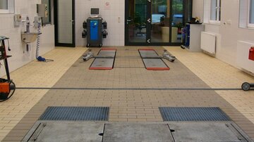 Eine saubere Werkstatt mit Hebebühnen und einem modernen Arbeitsplatz. Das Licht ist hell und die Wände sind weiß gefliest.