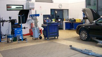 Eine Werkstatt mit verschiedenen Werkzeugen und Maschinen. Ein Auto steht in der Ecke, während der Boden gefliest ist.