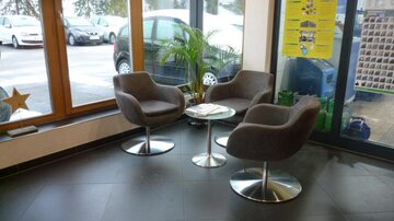 Ein moderner Wartebereich mit zwei bequemen Stühlen und einem kleinen Tisch. Große Fenster lassen viel Licht hereinfällen und bieten einen Blick nach draußen.