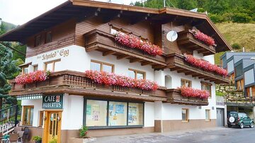 Ein charmantes Haus mit blühenden Blumenkästen und einer einladenden Cafétür. Im Hintergrund sind grüne Hügel zu sehen.