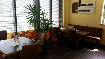 Ein gemütliches Restaurant mit modernen Möbeln und großen Fenstern. Die hellen Farben und Pflanzen schaffen eine einladende Atmosphäre.