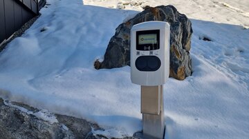 Ein digitaler Zähler steht auf einem schneebedeckten Untergrund neben einem Stein. Die Umgebung zeigt eine winterliche Landschaft.