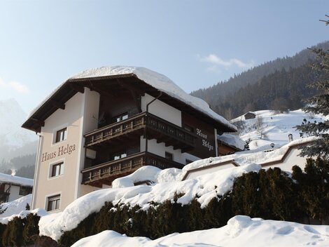 Ein gemütliches Haus in den Bergen, umgeben von Schnee und Tannen. Die schneebedeckte Landschaft strahlt Ruhe und Schönheit aus.