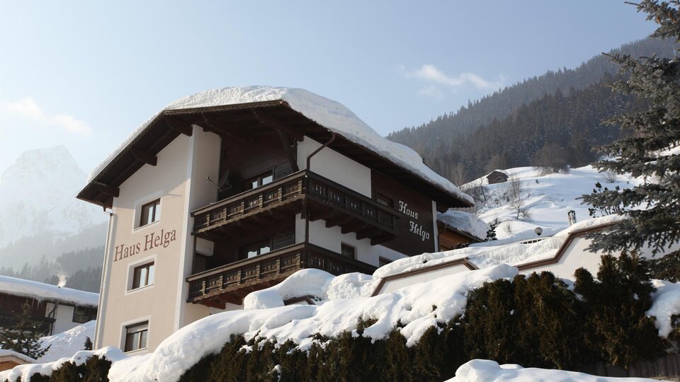 Ein gemütliches Haus in den Bergen, umgeben von Schnee und Tannen. Die schneebedeckte Landschaft strahlt Ruhe und Schönheit aus.