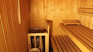 Eine gemütliche Sauna mit holzverkleideten Wänden und Bänken. Ein Eimer und eine Kelle stehen bereit für den Aufguss.