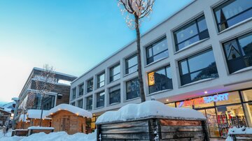Ein modernes Gebäude im Schnee mit großen Fenstern. Die Umgebung ist winterlich und ein wenig dekoriert.