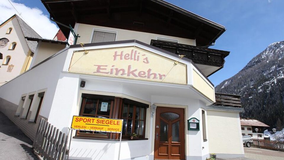 Ein gemütliches Gasthaus namens "Hell's Einkehr" in den Bergen. Die Fassade ist freundlich gestaltet und es gibt einen Blick auf die umliegenden Berge.