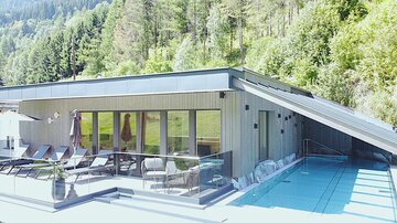 Ein modernes Haus mit einer großen Terrasse und einem Pool. Umgeben von grünen Bäumen und einer schönen Landschaft.