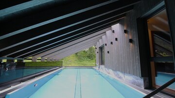 Ein moderner Innenpool in einem architektonisch ansprechenden Raum. Das große Fenster bietet einen Blick auf die grüne Umgebung.