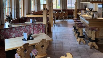 Ein gemütliches Restaurant mit Holzmöbeln und blühenden Sitzgelegenheiten. Große Fenster sorgen für viel Tageslicht und eine einladende Atmosphäre.