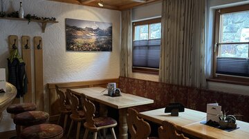 Ein gemütlicher Gastraum mit Holztischen und -stühlen. An der Wand hängt ein Bild einer Berglandschaft.