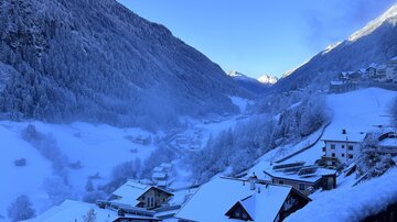 Eine schneebedeckte Berglandschaft mit kleinen, ruhigen Häusern. Der Himmel ist klar und blau, und die Landschaft strahlt eine friedliche Winterstimmung aus.