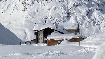 Ein gemütliches Chalet, umgeben von tiefem Schnee und majestätischen Bergen. Der Himmel ist klar und die Landschaft strahlt Ruhe aus.