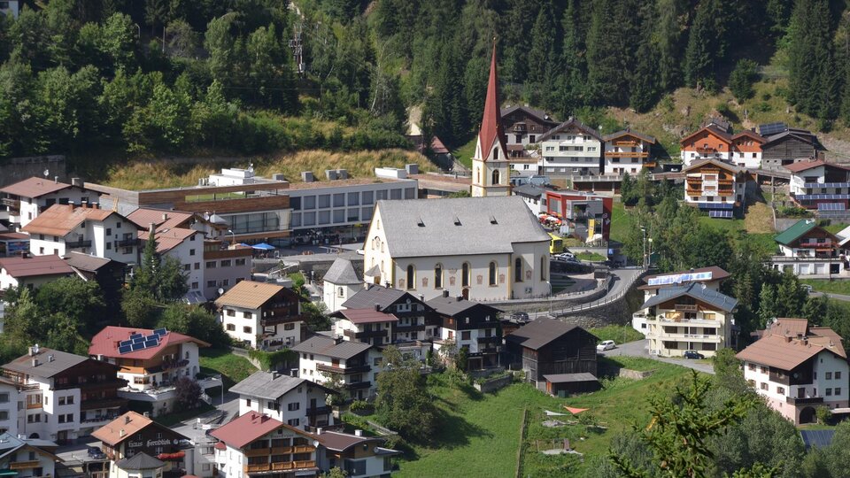 Eine malerische Bergstadt mit traditionellen Häusern und einer markanten Kirche. Umgeben von grünen Wiesen und dichten Wäldern.