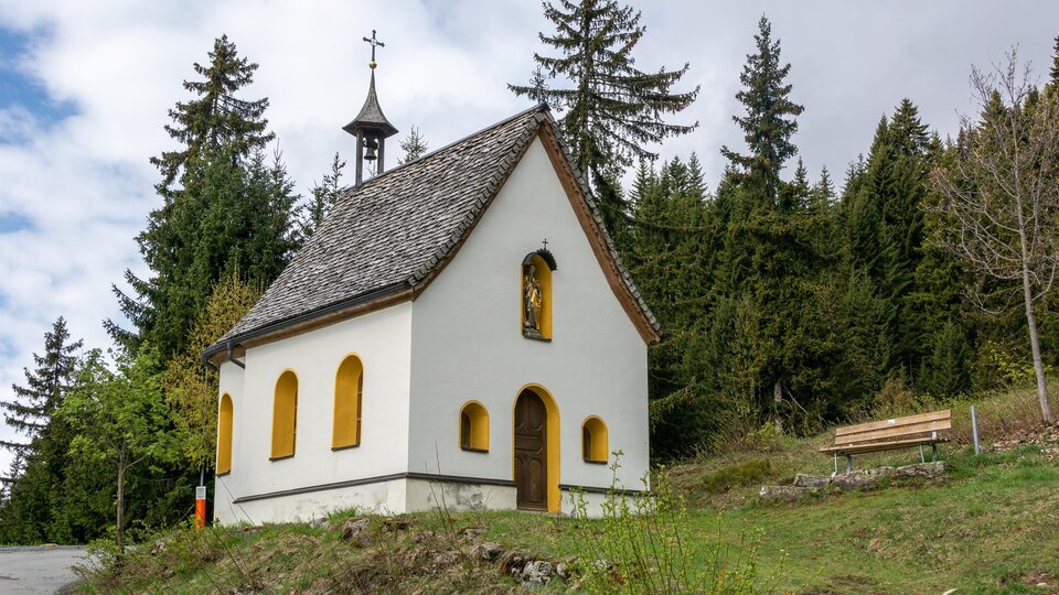 Eine kleine, weiße Kapelle steht inmitten von Bäumen. Der Himmel ist bewölkt und die Umgebung ist grün. | © Bernhard Gruber – Photography