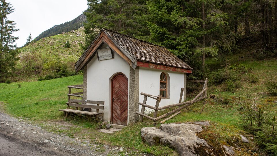 Eine kleine, malerische Hütte steht inmitten einer grünen Landschaft. Umgeben von Bäumen und Bergen bietet sie eine ruhige Atmosphäre. | © Bernhard Gruber – Photography