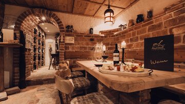 Eine gemütliche Weinstube mit Holztisch und dekadentem Essen. Die Wände aus Ziegelstein und sanfte Beleuchtung schaffen eine einladende Atmosphäre.