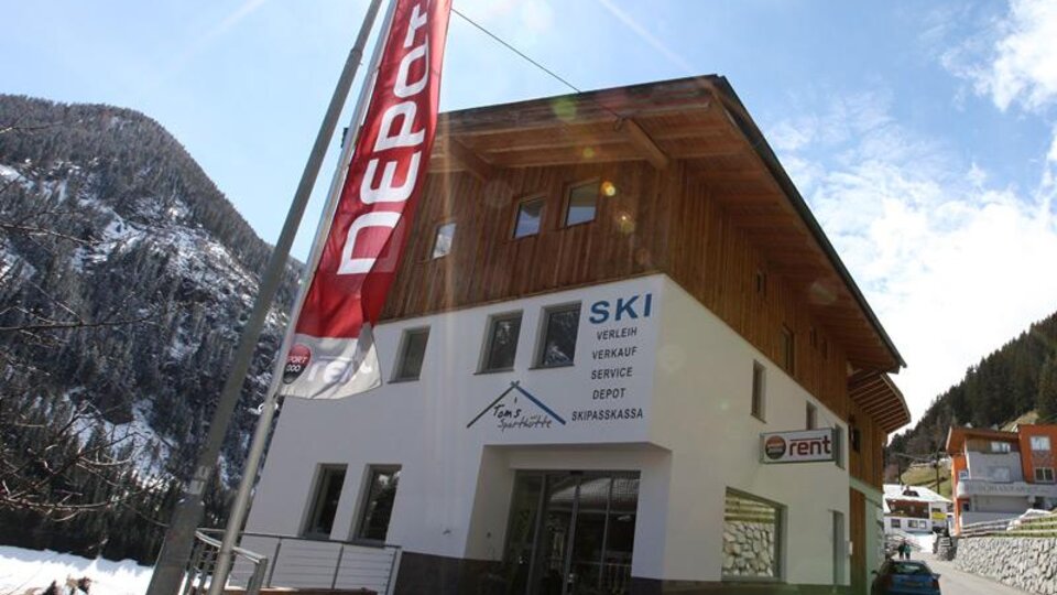 Ein modernes Geschäft mit Holzfassade, das Ski-Verleih und -Verkauf anbietet. Die Umgebung ist bergig und schneebedeckt.